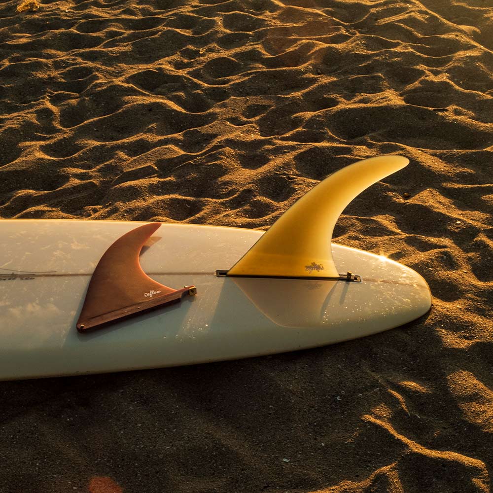 Quilla single fin Deflow Cream montada sobre longboard sobre la arena.