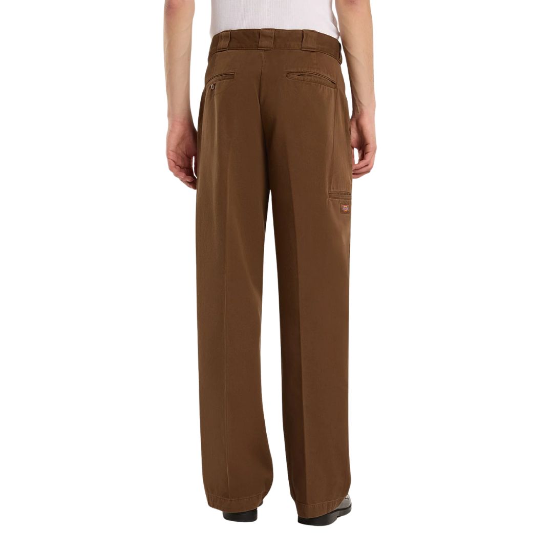 Pantalón Dickies 247 Loose GD en marrón Timber sobre modelo visto de espalda, con las manos en los bolsillos traseros ribeteados y el bolsillo lateral con etiqueta Dickies visible.