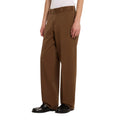 Vista lateral del pantalón Dickies 247 Loose GD en marrón Timber sobre modelo, mostrando el corte holgado de pierna recta y la caída del bajo hasta el calzado.
