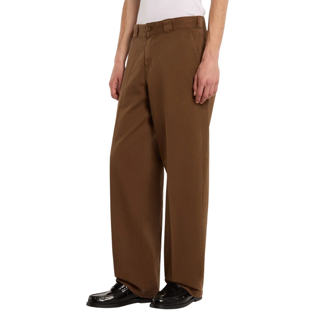Vista lateral del pantalón Dickies 247 Loose GD en marrón Timber sobre modelo, mostrando el corte holgado de pierna recta y la caída del bajo hasta el calzado.