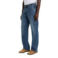 Modelo con vaqueros Dickies 954 Relaxed Straight Work Jeans classic blue en vista lateral tres cuartos, de corte relaxed y pierna recta, con bolsillo delantero y zapatillas.
