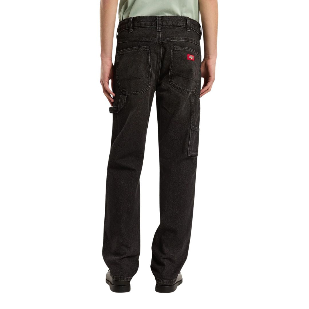 Vista trasera de modelo con vaqueros Dickies 993 Regular Tapered Carpenter black, con etiqueta roja en el bolsillo, trabilla para martillo y bolsillo utilitario en la pierna.