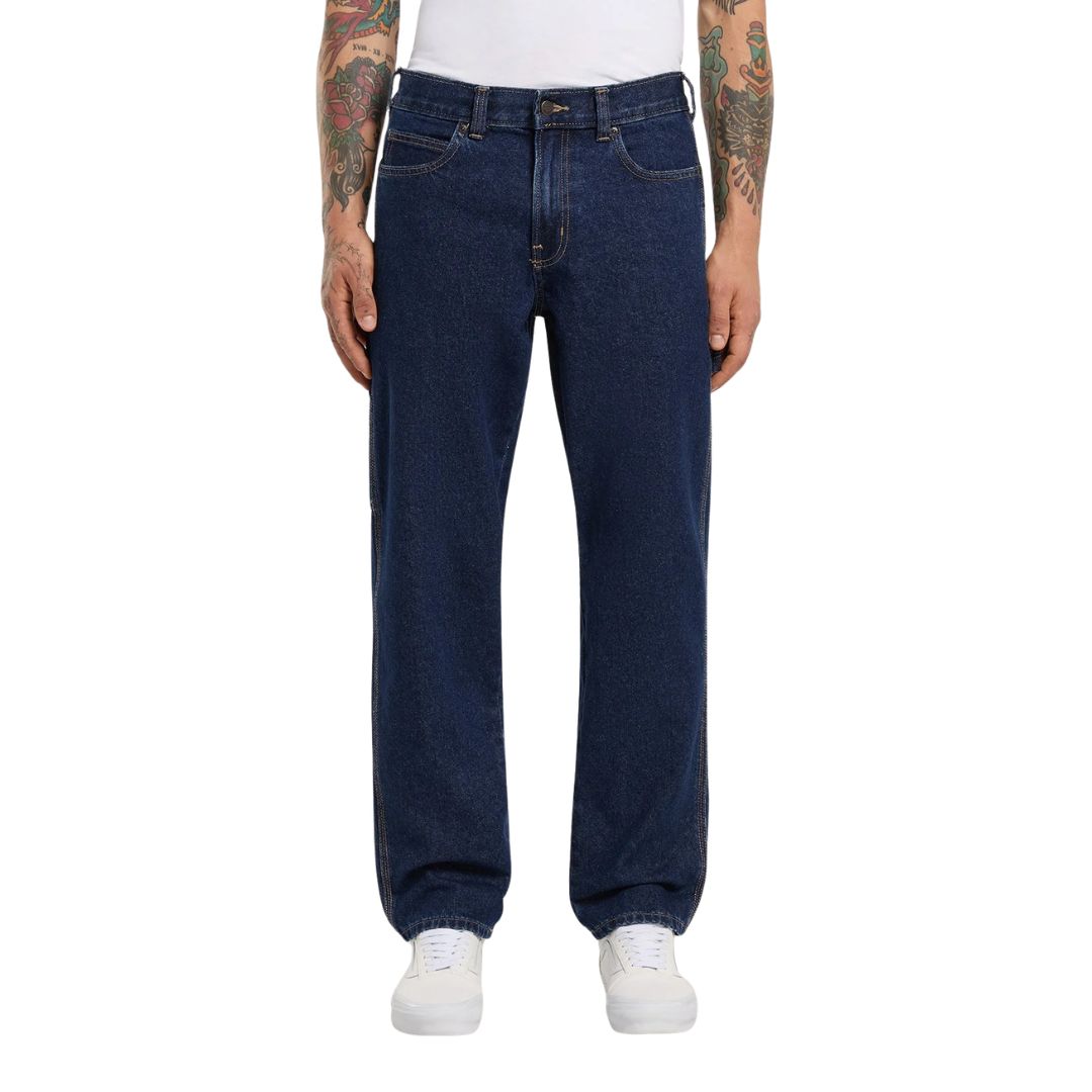 Vista frontal de modelo con vaqueros Dickies 993 Regular Tapered Carpenter dark indigo de pierna recta, con botón metálico, cinco bolsillos y zapatillas blancas.