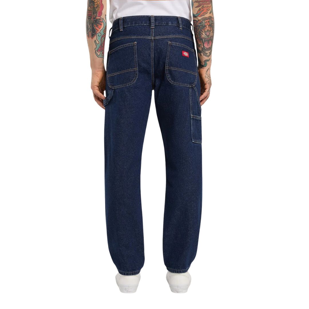 Vista trasera de modelo con vaqueros Dickies 993 Regular Tapered Carpenter dark indigo, con etiqueta roja Dickies, bolsillos de parche y bolsillo utilitario lateral.