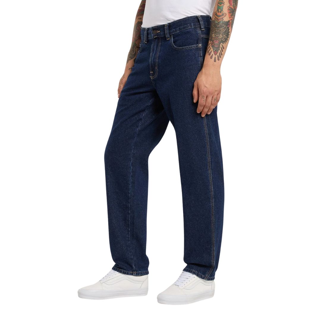 Modelo con vaqueros Dickies 993 Regular Tapered Carpenter dark indigo en vista lateral tres cuartos, con bolsillo delantero, costura lateral y zapatillas blancas.