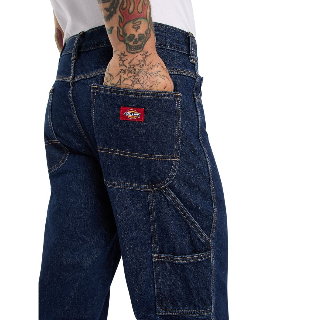 Primer plano del bolsillo trasero con etiqueta roja Dickies y del bolsillo utilitario de los vaqueros 993 Regular Tapered Carpenter dark indigo, con costuras en contraste.