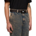 Cinturón Dickies Orcutt Webbing Belt en marrón oscuro puesto sobre un vaquero holgado, ajustado a la cintura mediante el cierre de hebilla deslizante de metal.