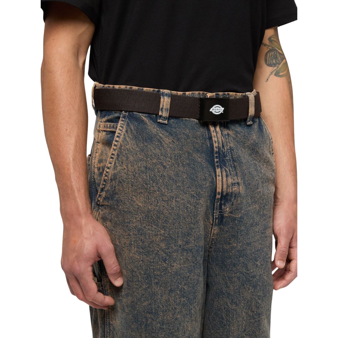 Cinturón Dickies Orcutt Webbing Belt en marrón oscuro puesto sobre un vaquero holgado, ajustado a la cintura mediante el cierre de hebilla deslizante de metal.