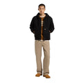 Modelo de cuerpo entero con chaqueta Dickies Hilham Hooded Canvas negra combinada con pantalón beige.