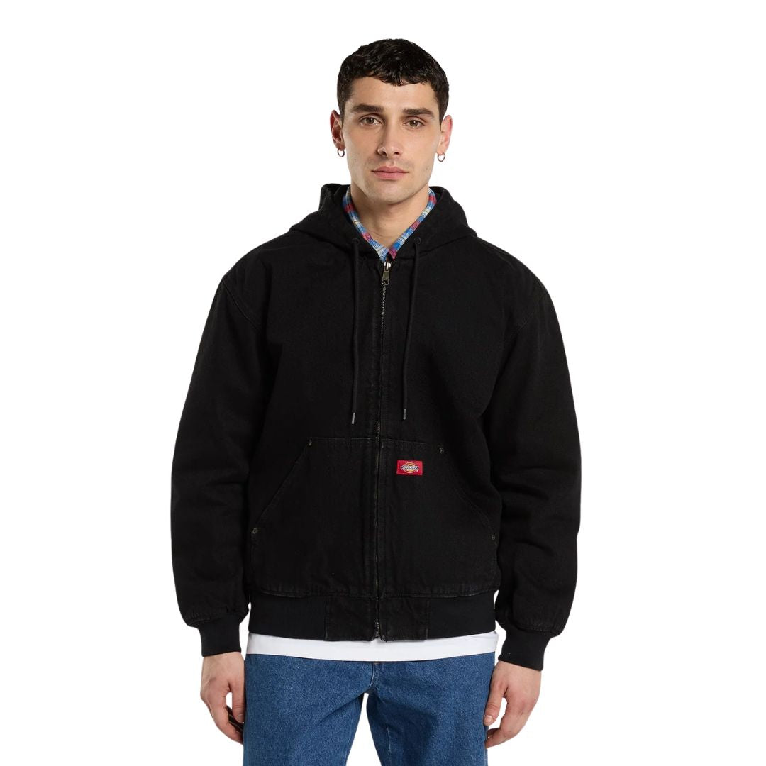 Modelo de frente con la Dickies Hilham LN DNM Hood Bomber vaquera negra con capucha, cordones colgando, cremallera cerrada, bolsillo canguro con etiqueta roja y puños acanalados.