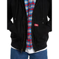 Detalle del bolsillo canguro con remaches y etiqueta roja de la Dickies Hilham LN DNM Hood Bomber vaquera negra, con las manos en los bolsillos, cremallera abierta y bajo acanalado.