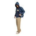Modelo de cuerpo entero con la Dickies Hilham LN DNM Hood Bomber vaquera azul lavado, capucha puesta y cremallera abierta, sobre camiseta Dickies, pantalón chino beige y zapatillas.