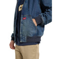 Detalle del bolsillo canguro con remaches y etiqueta tejida de la Dickies Hilham LN DNM Hood Bomber, chaqueta vaquera azul lavado, con la mano dentro y puño acanalado azul marino.