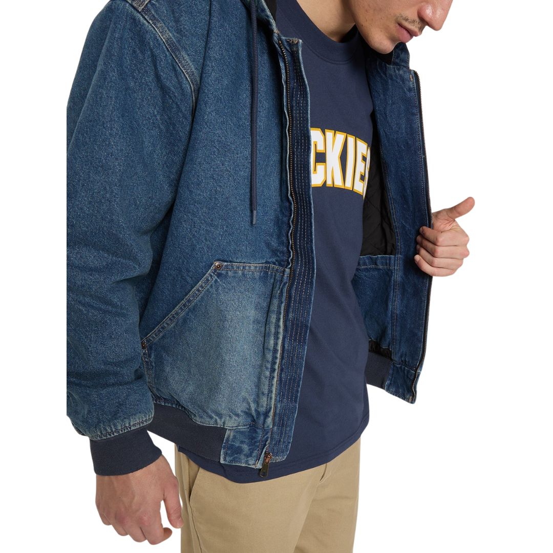Modelo con la Dickies Hilham LN DNM Hood Bomber vaquera azul lavado abierta, mostrando el forro acolchado de rombos, bolsillo canguro con remaches y camiseta Dickies azul marino.