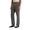 Modelo vistiendo el pantalón Dickies Houston Denim Grey Wash Tinted gris lavado con camiseta beige y zapatillas negras.