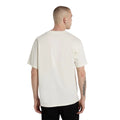 Modelo de espaldas con la Dickies McDermitt SS Tee, camiseta boxy blanca crudo de manga corta y espalda lisa, sobre un pantalón vaquero negro ancho.