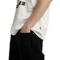Detalle del bajo de la Dickies McDermitt SS Tee blanca crudo, con la etiqueta tejida Dickies cosida en la costura lateral, sobre un pantalón vaquero negro.