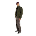 Modelo de cuerpo entero con la Dickies Mount Hope Fleece verde oliva, camisa negra, vaqueros grises anchos, gorro granate y zapatillas negras y blancas, con una mano en el bolsillo.