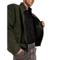 Modelo con la Dickies Mount Hope Fleece verde oliva abierta sobre camisa negra, mostrando el forro interior liso, la cremallera y la mano en el bolsillo de unos vaqueros grises.