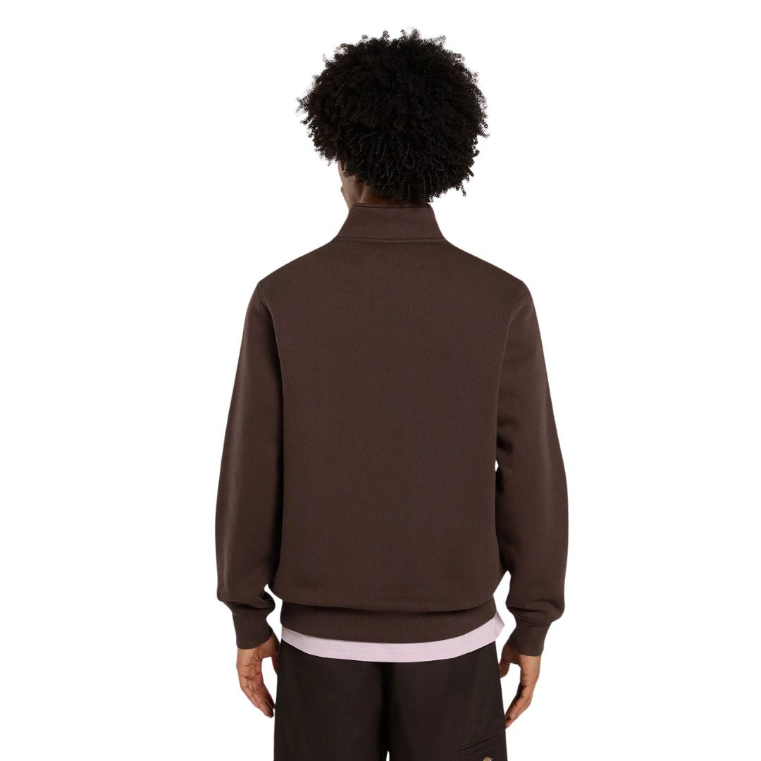 Vista trasera de un modelo con la sudadera Dickies Oakport Quarter Zip marrón chocolate, mostrando la espalda lisa, el cuello alto y el canalé de la cintura sobre camiseta rosa.