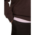 Detalle del puño y la cintura de canalé de la sudadera Dickies Oakport Quarter Zip marrón chocolate, con la mano en el bolsillo del pantalón y camiseta rosa lavanda debajo.