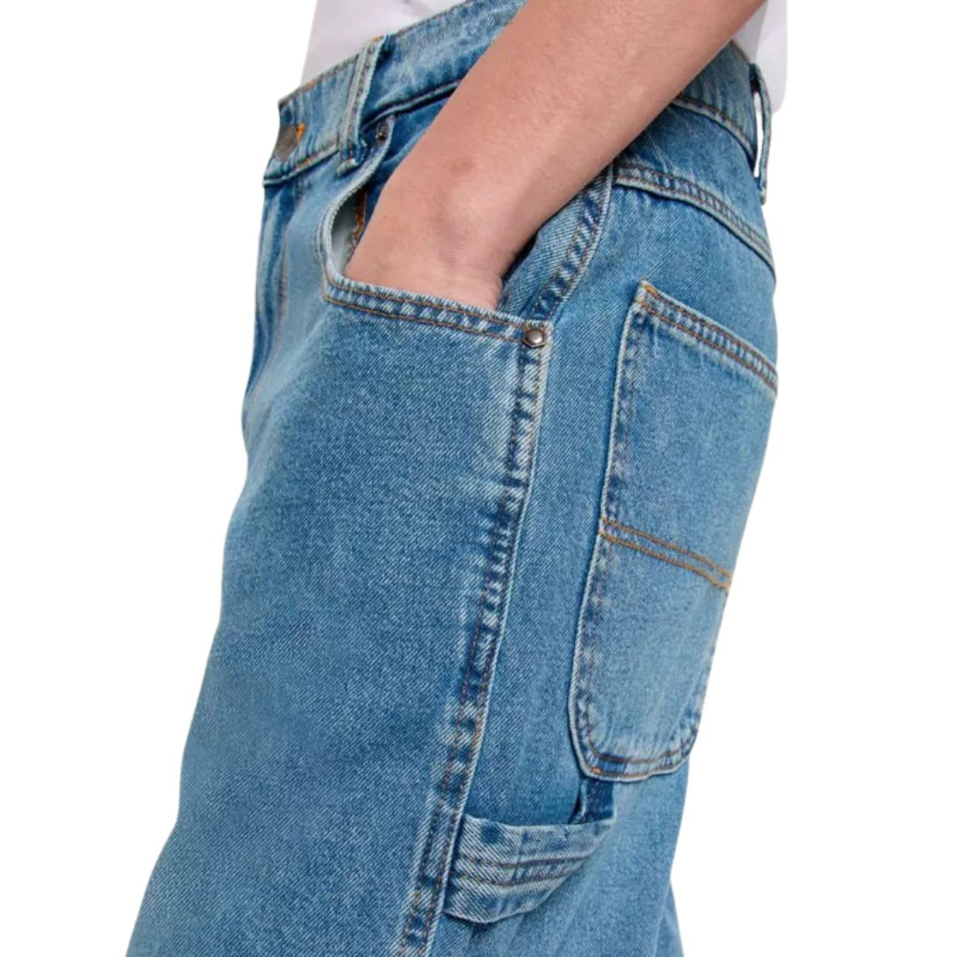 Vista lateral del pantalón Dickies Garyville Denim Rinsed Fade mostrando los bolsillos tipo carpintero y la textura del denim azul.