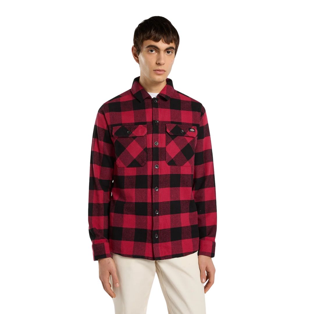 Modelo de frente con la Dickies Sacramento Shirt roja y negra completamente abrochada, mostrando los dos bolsillos en el pecho, sobre un pantalón chino beige.
