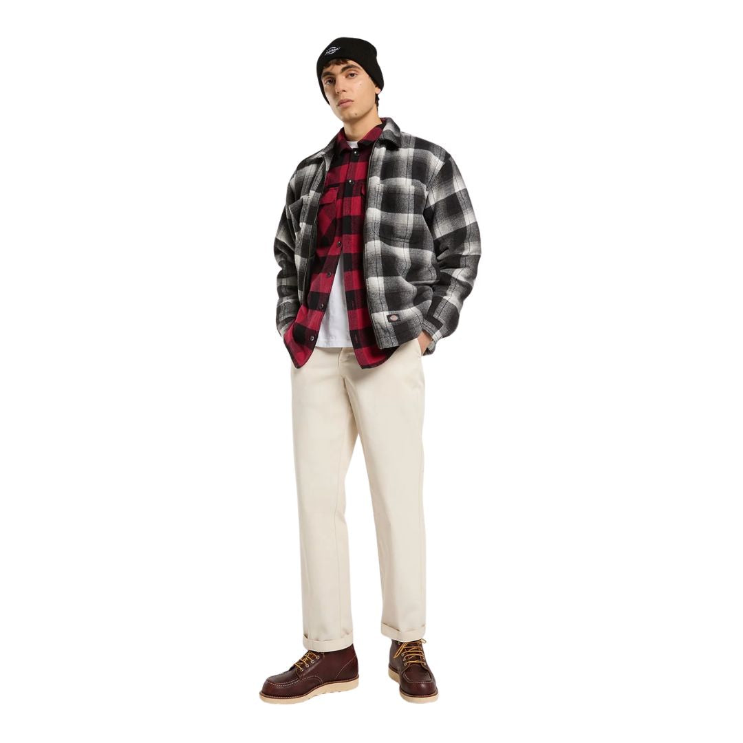 Modelo con la Dickies Sacramento Shirt roja y negra bajo una camisa de cuadros gris y negra abierta, gorro Dickies, pantalón chino beige y botas de piel marrones.