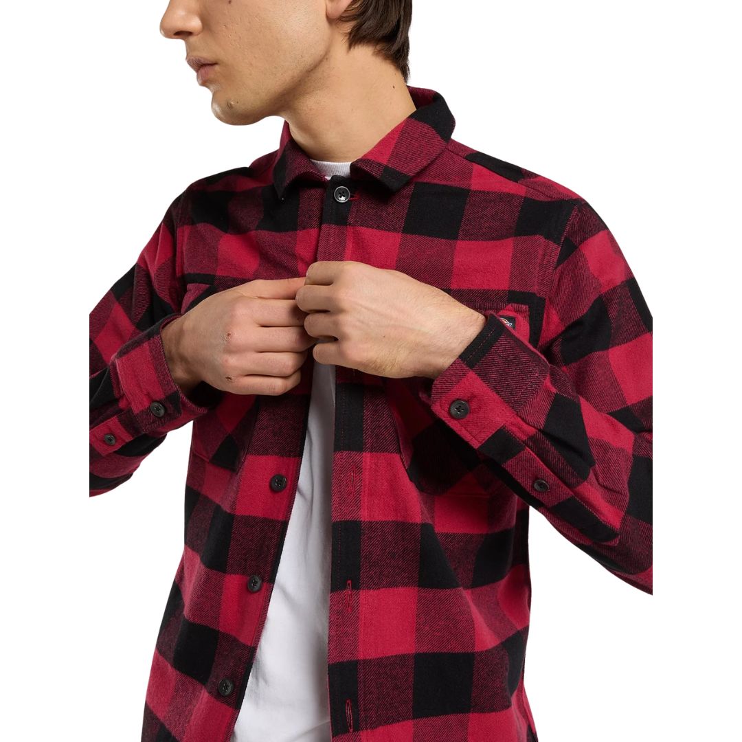Detalle del cuello y los botones de la Dickies Sacramento Shirt, camisa de franela a cuadros roja y negra de algodón, con la mano abrochando el botón del cuello.