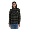 Modelo de frente con la Dickies Sacramento Shirt verde oliva y negro completamente abrochada, mostrando los dos bolsillos en el pecho, sobre pantalón vaquero azul.