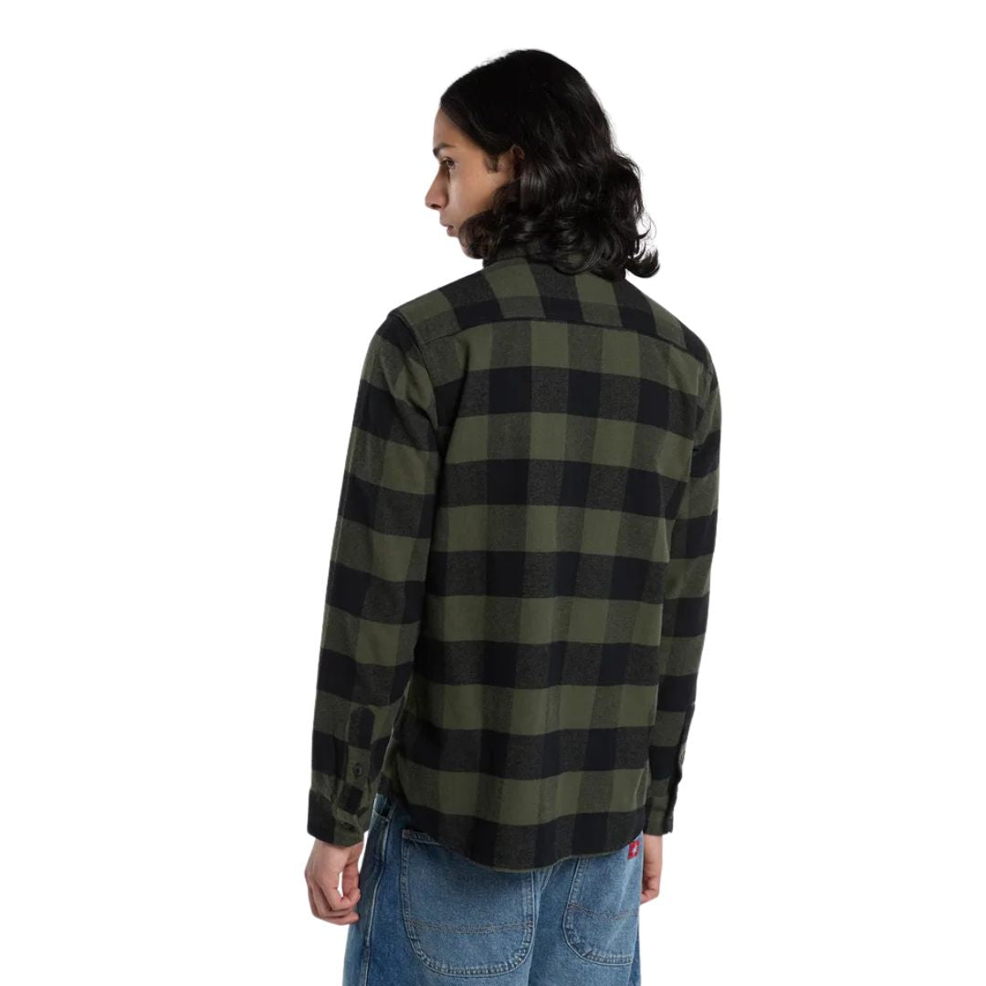 Modelo de espaldas con la Dickies Sacramento Shirt, camisa de franela a cuadros verde oliva y negro de manga larga, sobre pantalón vaquero azul holgado.