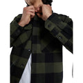 Detalle del cuello de la Dickies Sacramento Shirt, camisa de franela a cuadros verde oliva y negro de algodón, con la mano abrochando el botón del cuello.