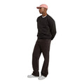 Modelo con la Dickies Sutcliffe Sweatshirt marrón oscuro, gorra rosa, pantalón vaquero marrón oscuro y zapatillas blancas, en un plano de cuerpo entero de perfil.