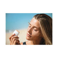Mujer aplicando protector solar en stick EQ SPF50+ bio en el rostro en la playa con alta protección solar para zonas sensibles.