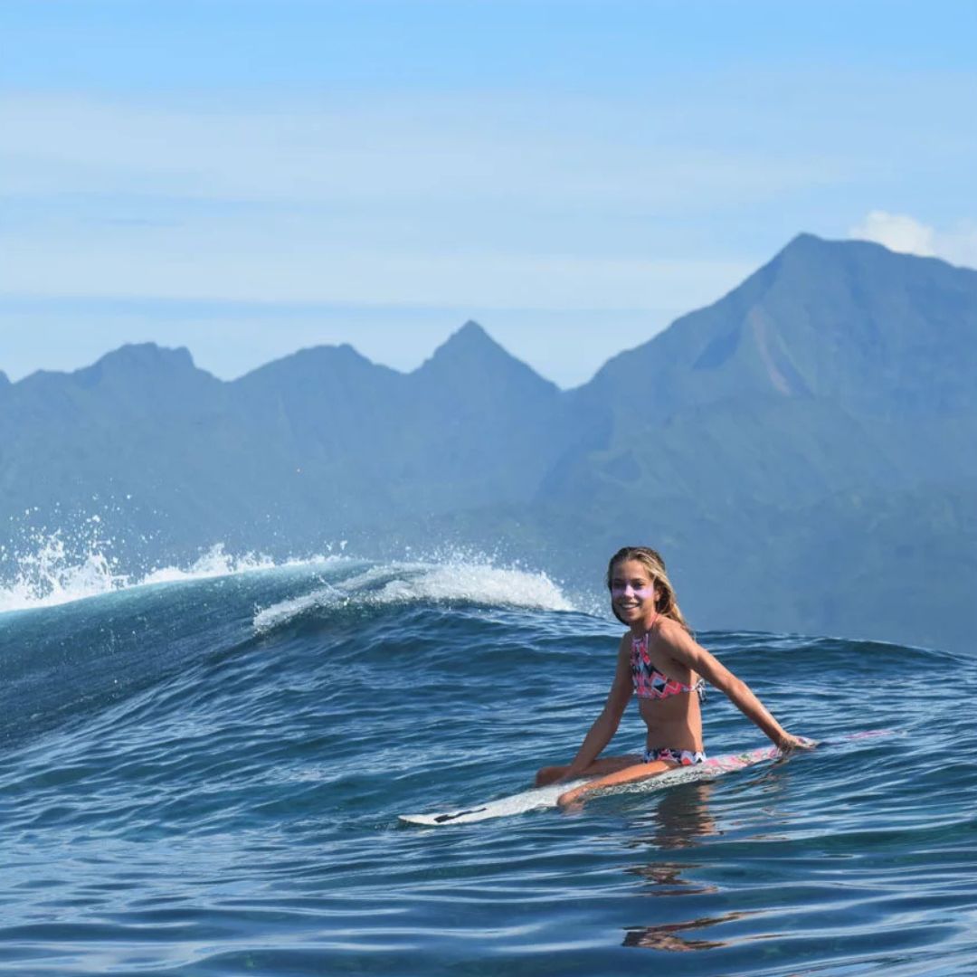 Mujer practicando surf con protector solar en stick EQ SPF50+ bio color mauve aplicado en el rostro en el mar.