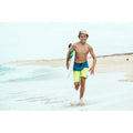 Niño surfista corriendo por la playa con protector solar turquesa en la cara usando stick SPF50+ resistente al agua.