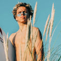 Joven surfista con protector solar turquesa en la cara usando stick solar SPF50+ bio resistente al agua en la playa.