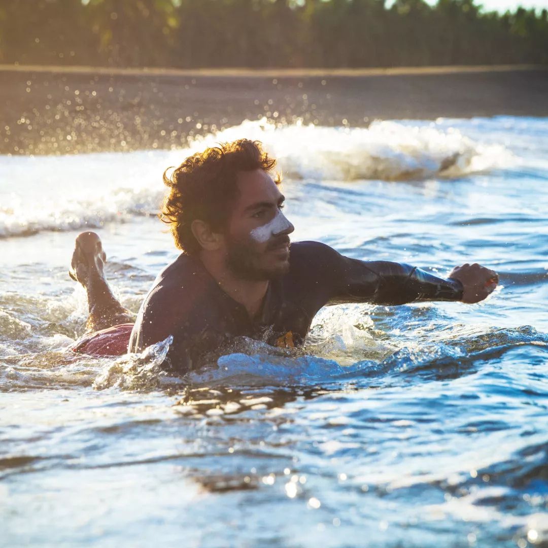 Hombre surfista con protector solar blanco en la cara usando stick solar SPF50+ bio resistente al agua en el mar.