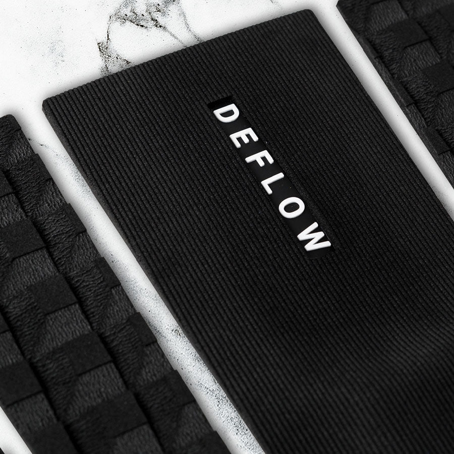 Detalle del grip de surf de tres piezas Deflow 3 Piece Pop Traction en color negro sobre tabla de surf.