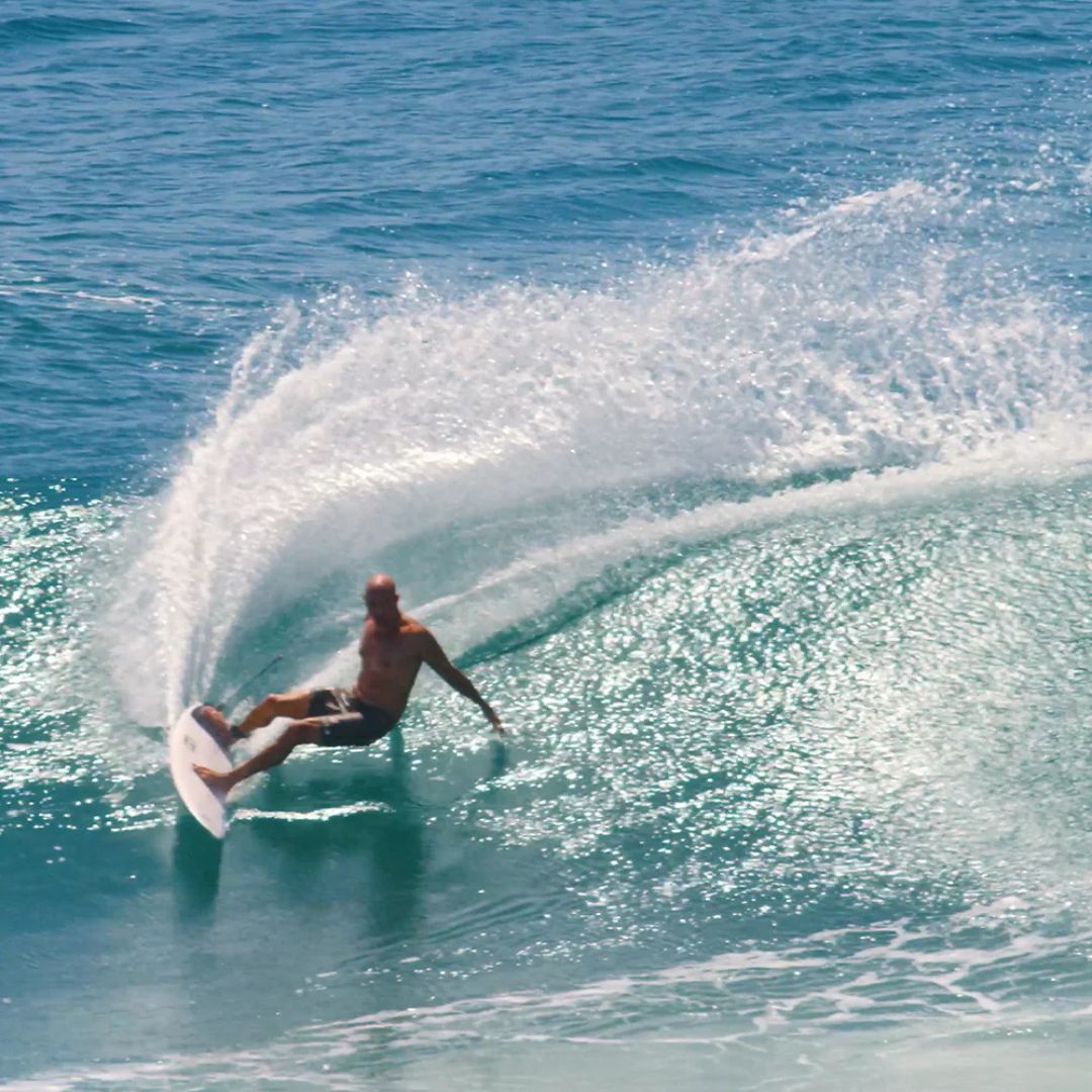 Kelly Slater trazando un giro amplio con gran proyección de agua en una ola, imagen de contexto de surf asociada al set de quillas Firewire Endorfins KSR.