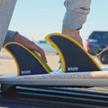 Instalación de dos quillas Firewire Spun Honey en los cajetines Futures traseros de una tabla de surf, sobre un portaequipajes.