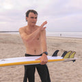 Surfista sujetando una tabla en la playa con el set de quillas Firewire Spun Honey ya instalado en los cajetines Futures.