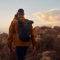 Hombre caminando al atardecer con mochila Fjällräven High Coast Foldsack 24 navy ajustada a la espalda