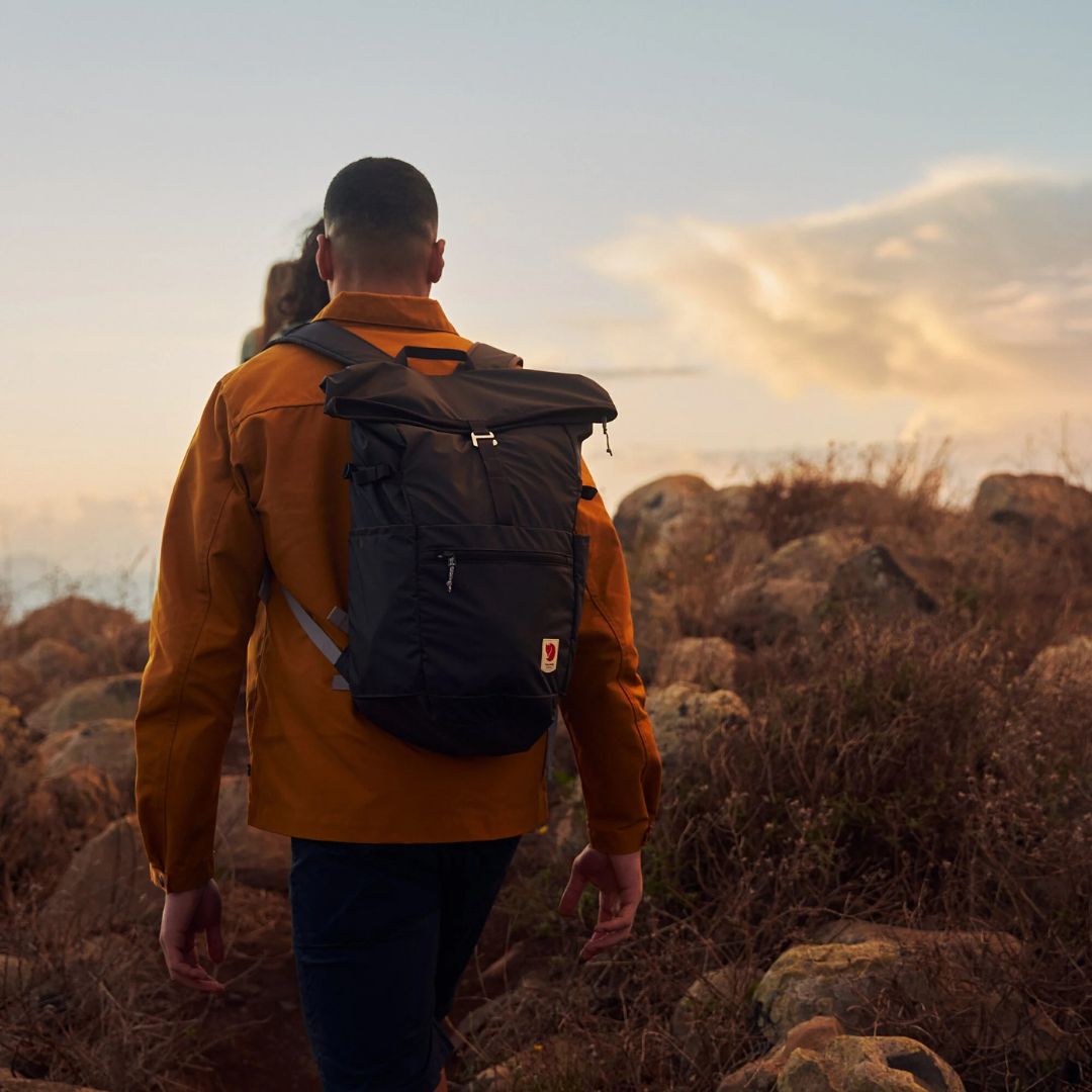 Hombre caminando al atardecer con mochila Fjällräven High Coast Foldsack 24 navy ajustada a la espalda