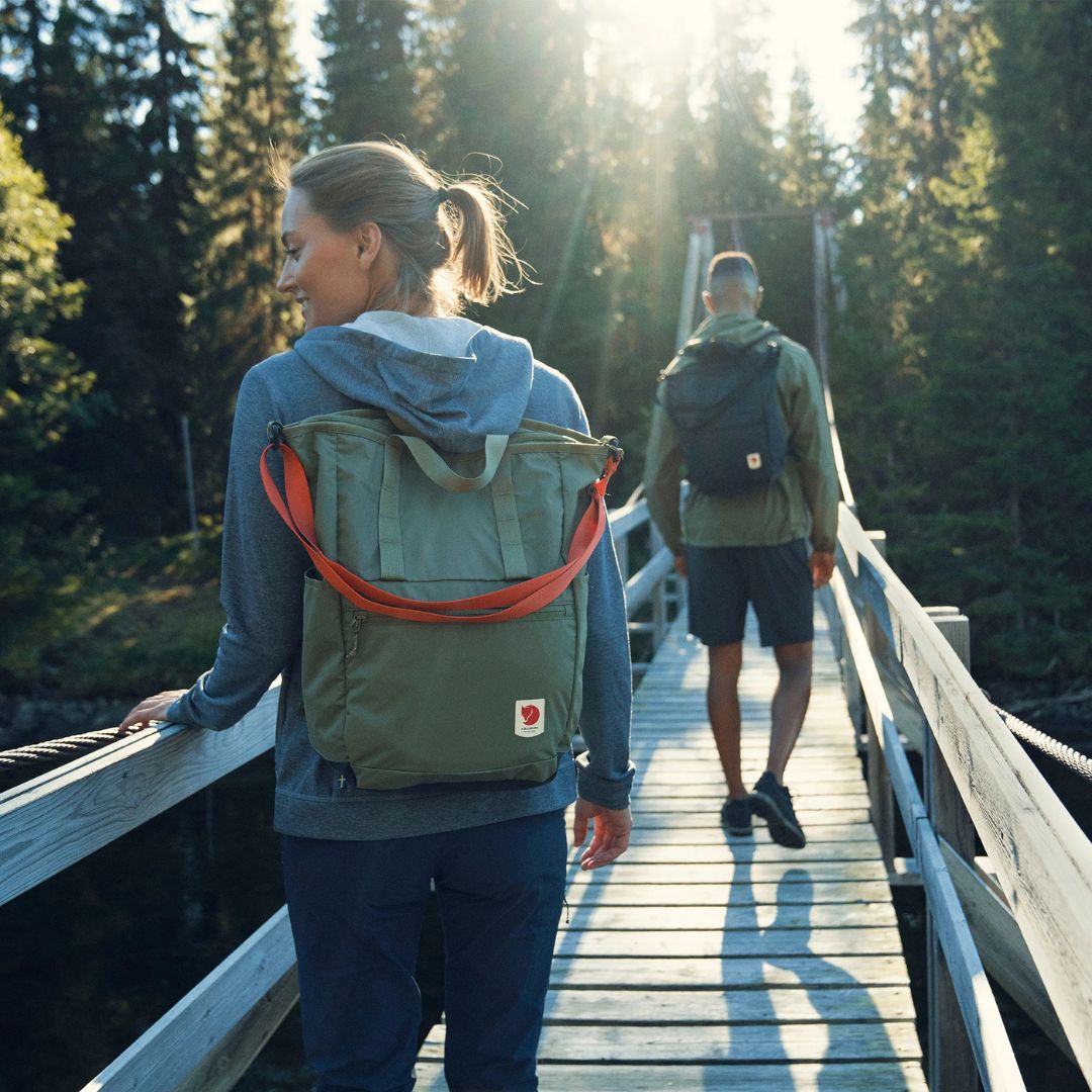 Personas caminando sobre un puente con mochilas Fjällräven High Coast Totepack en uso diario