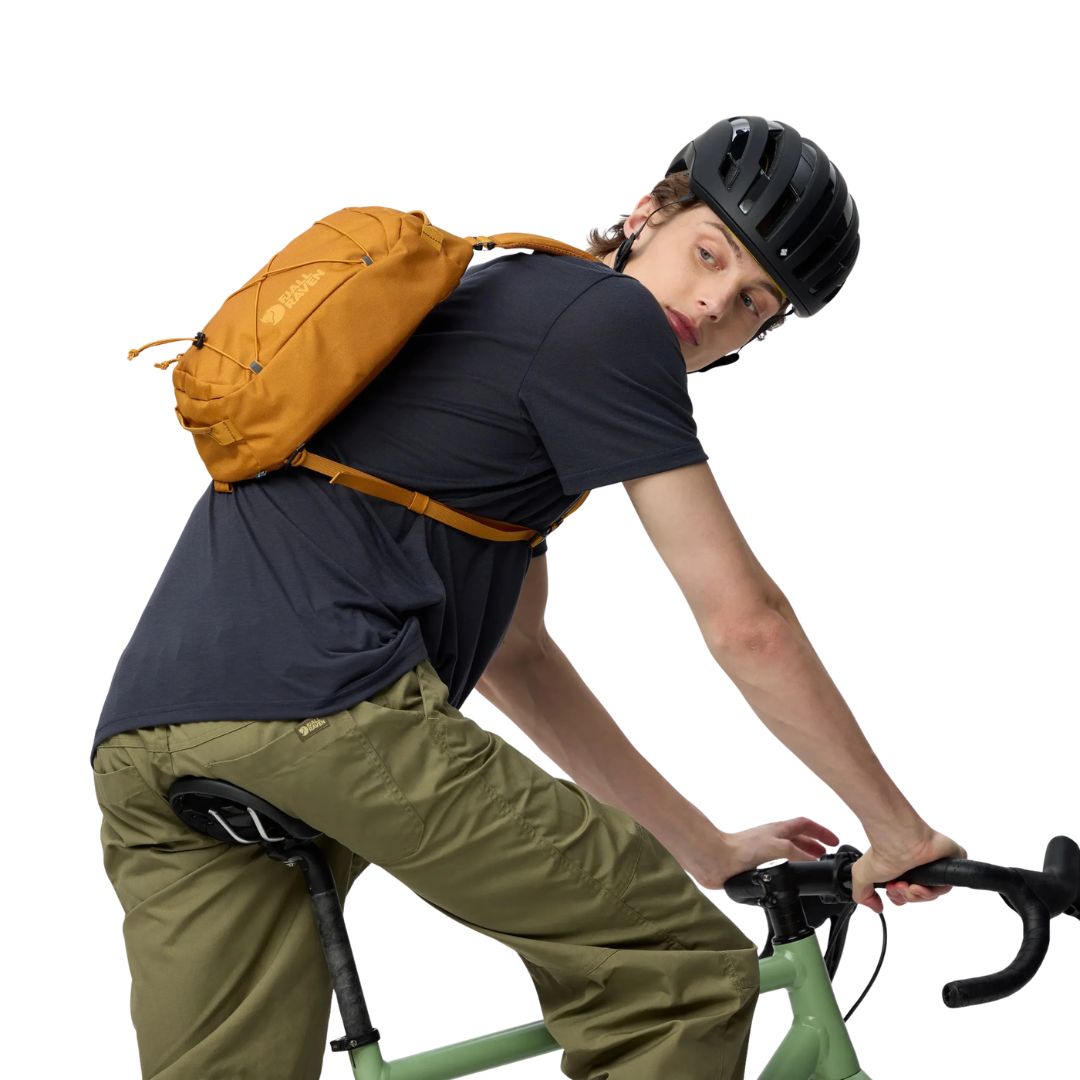 Bandolera Fjällräven Skule Sling 6 color mostaza usada en bicicleta, mochila cruzada urbana ligera de 6 litros con correa ajustable y diseño ergonómico.
