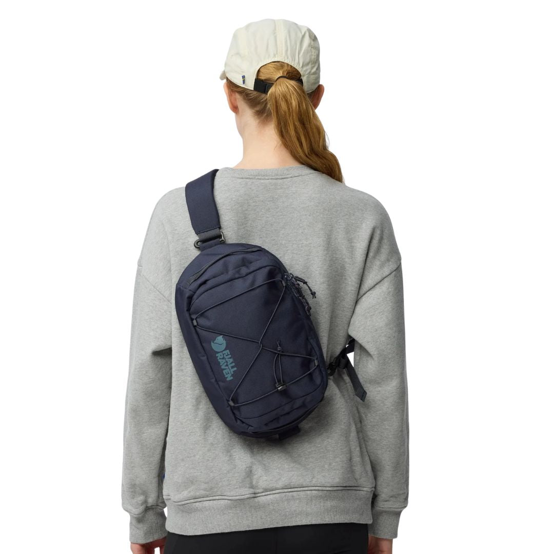Fjällräven Skule Sling 6 azul marino llevada cruzada en la espalda, bandolera urbana 6L con cordón elástico frontal y ajuste cómodo.