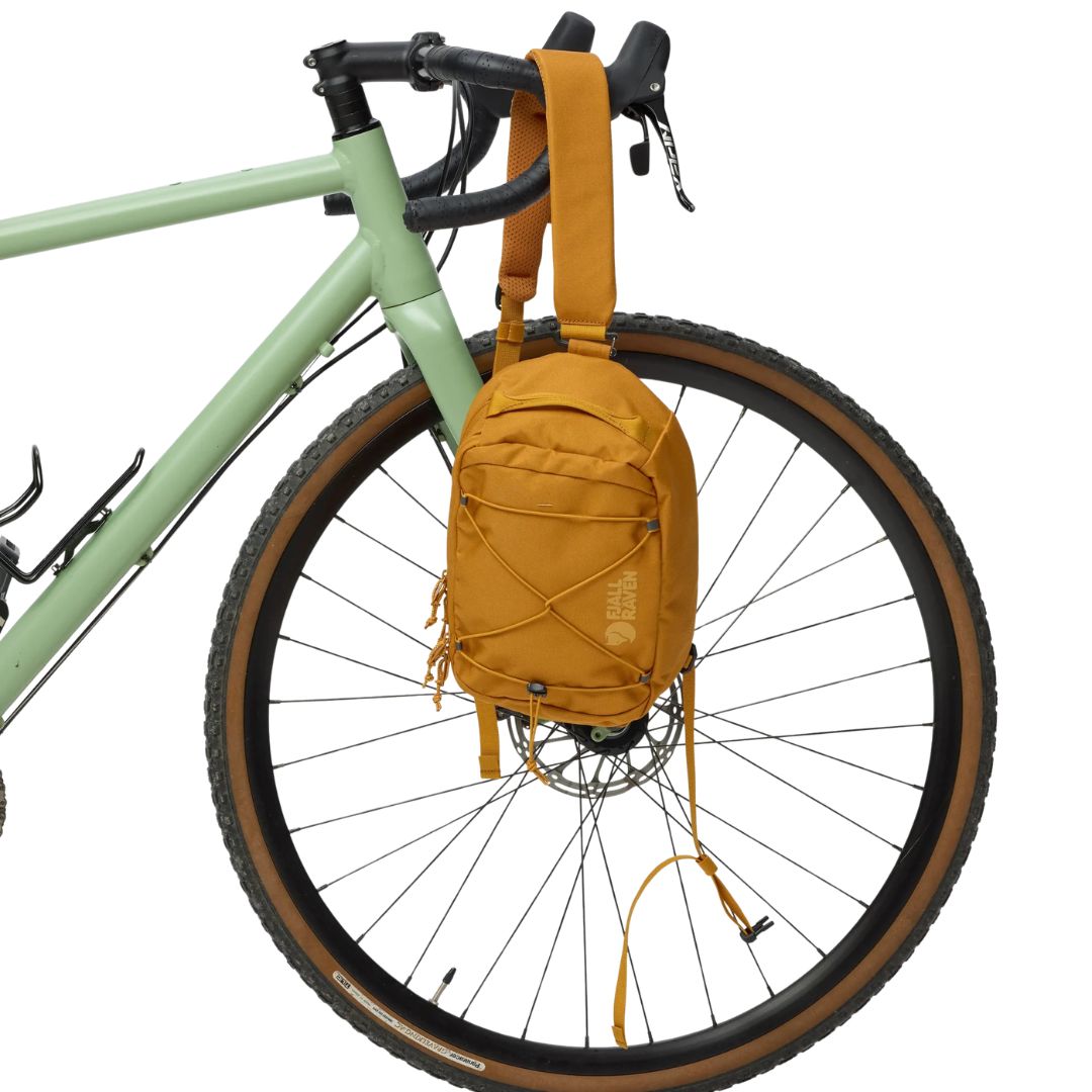 Bandolera Fjällräven Skule Sling 6 mostaza colgada en bicicleta, diseño compacto 6L con cordón elástico desmontable y tejido reciclado resistente.