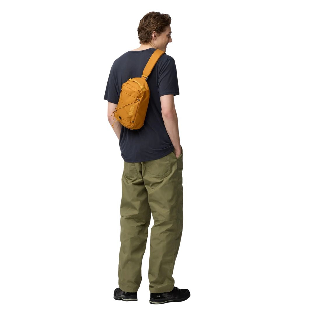 Bandolera Fjällräven Skule Sling 6 mostaza llevada cruzada, bolso urbano compacto 6L para uso diario y movilidad urbana.