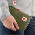 Bolso Fjällräven High Coast Pocket sostenido con la mano, mostrando su tamaño compacto y logotipo visible.